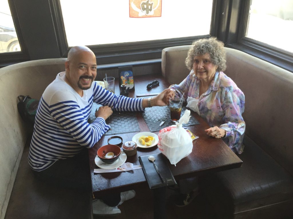 A younger man and older woman are in a booth at a restaurant. They hold hands across the table.