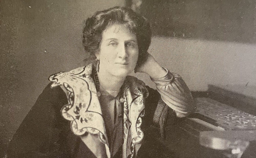 Photograph portrait of Liza Lehmann leaning her elbow on a piano.