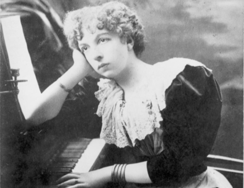 Cécile Chaminade leaning her elbow over a piano and looking off to the left. The photo is in black and white.