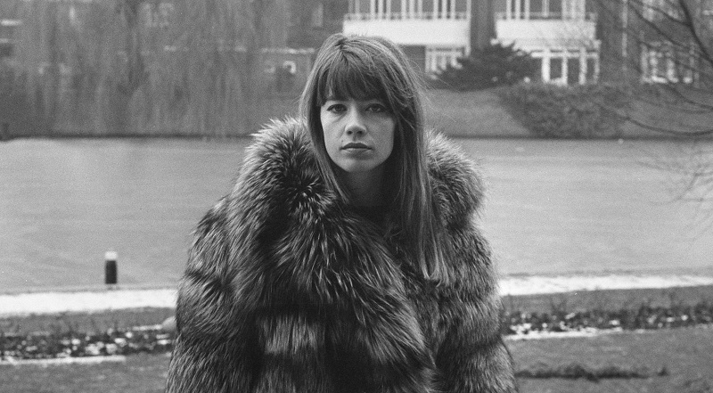 Picture of Françoise Hardy in black-and-white. She wears a fluffy fur coat standing in front of a body of water.