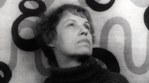 A black-and-white photo of Lotte Lenya. She is pictured from the neck up looking up to the right with 70's-patterned walls behind her.